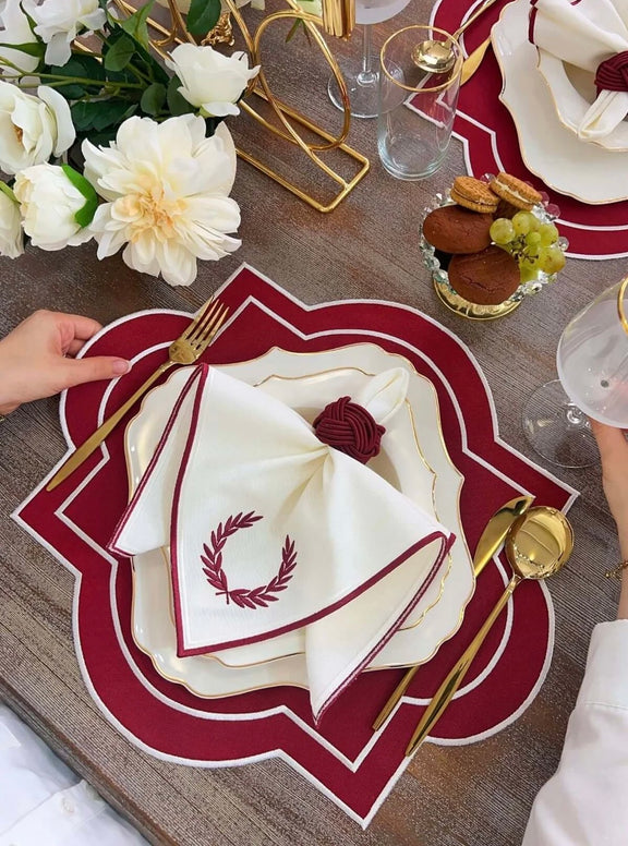 Sophisticated Milan Design table set with red embroidered placemats and napkins. Features waterproof fabric and gold-accented dining accessories.